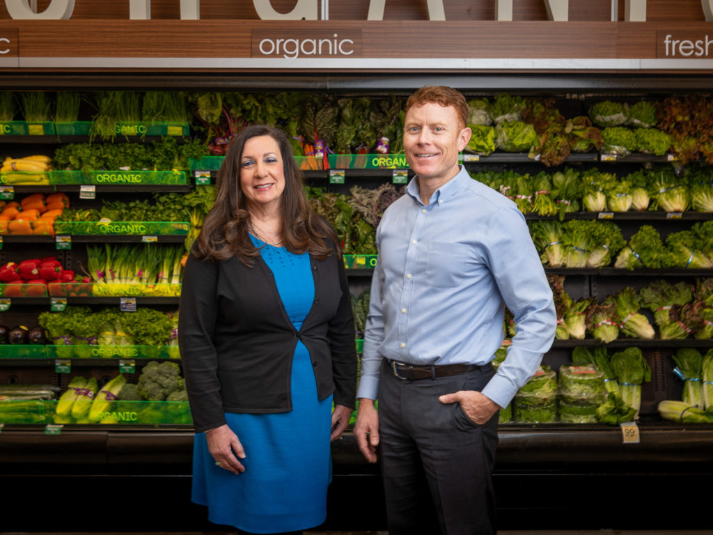 Woman and man stand in front of produce at a Safeway store