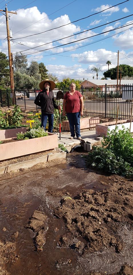 Image shows a man and a woman in their raised bed garden which uses irrigation.