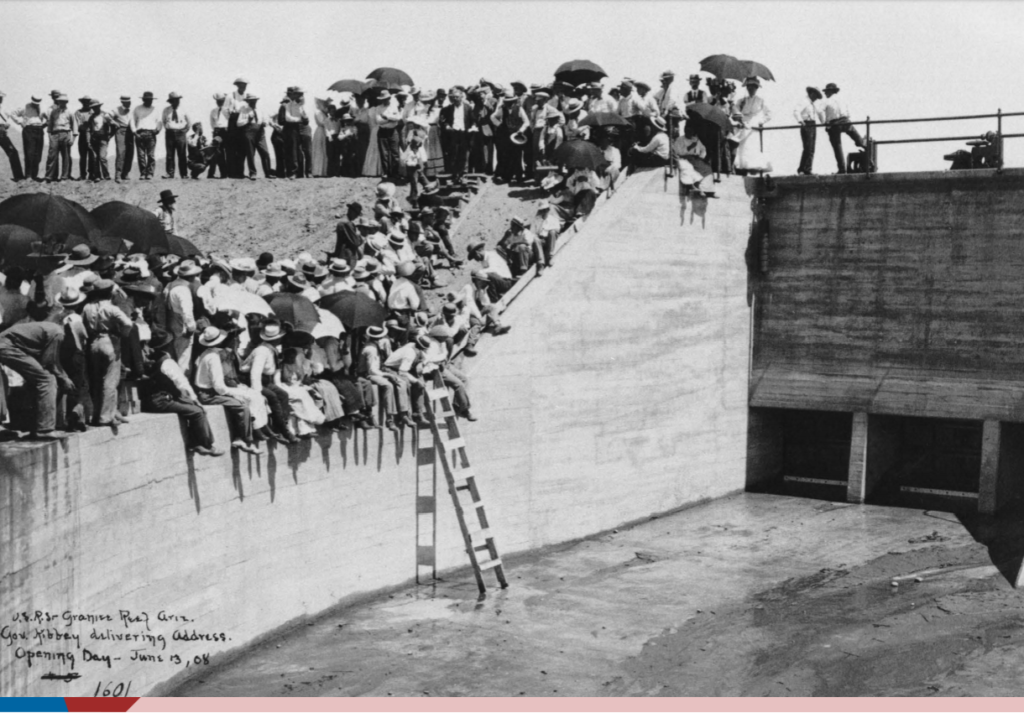 Image shows a large concrete wall with people sitting on it.