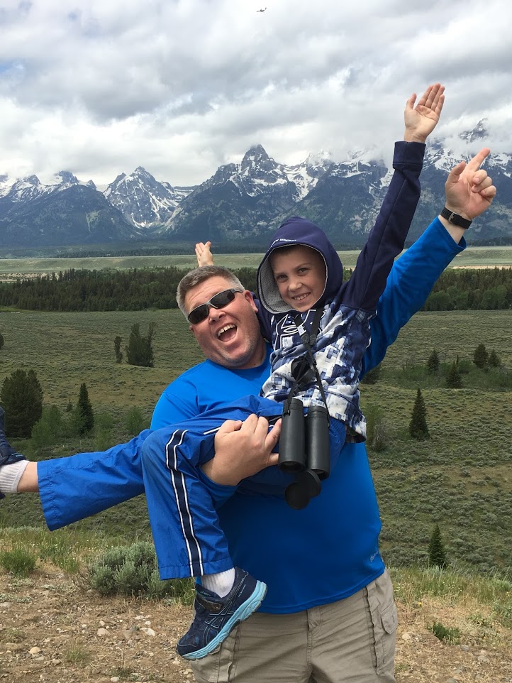 Image shows a father and son posing with arms out and with smiles on their faces