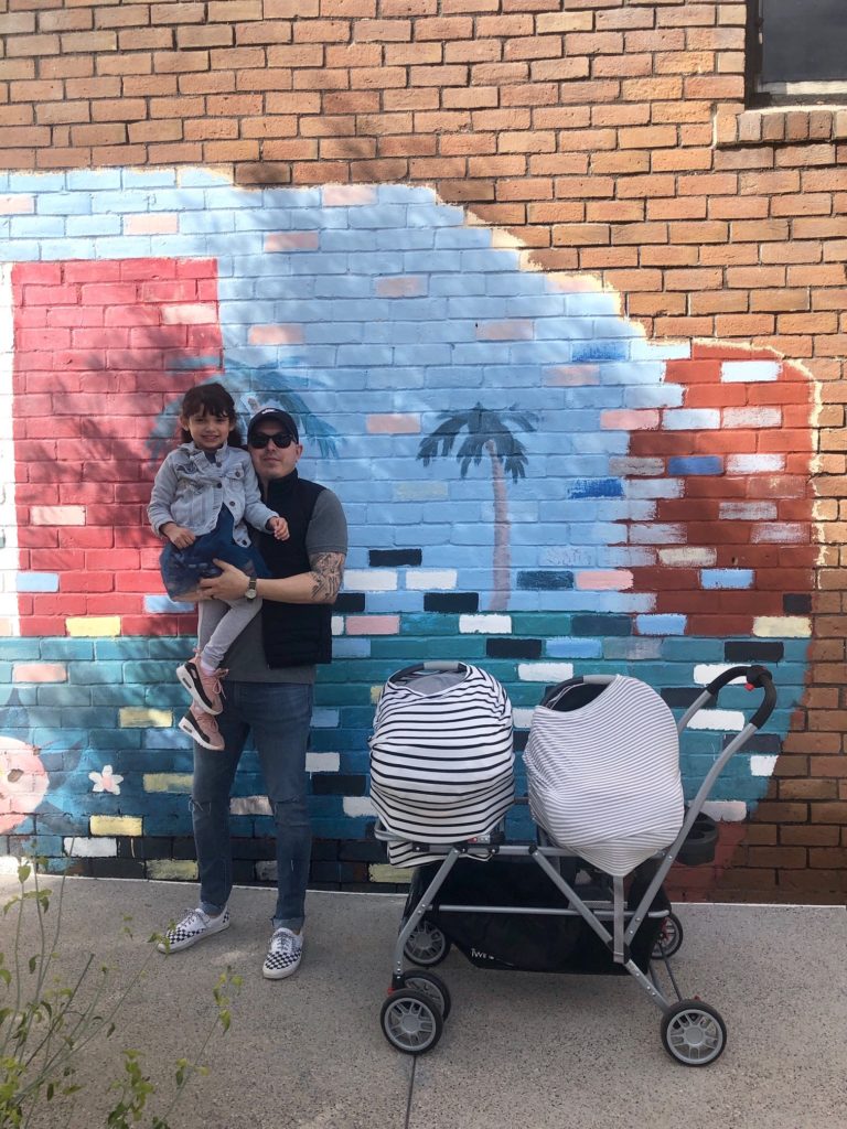 Image shows a father holding a daughter with a double stroller.