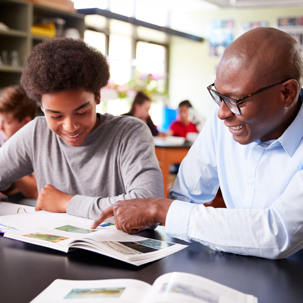 Image shows a male teacher sitting next to a male student